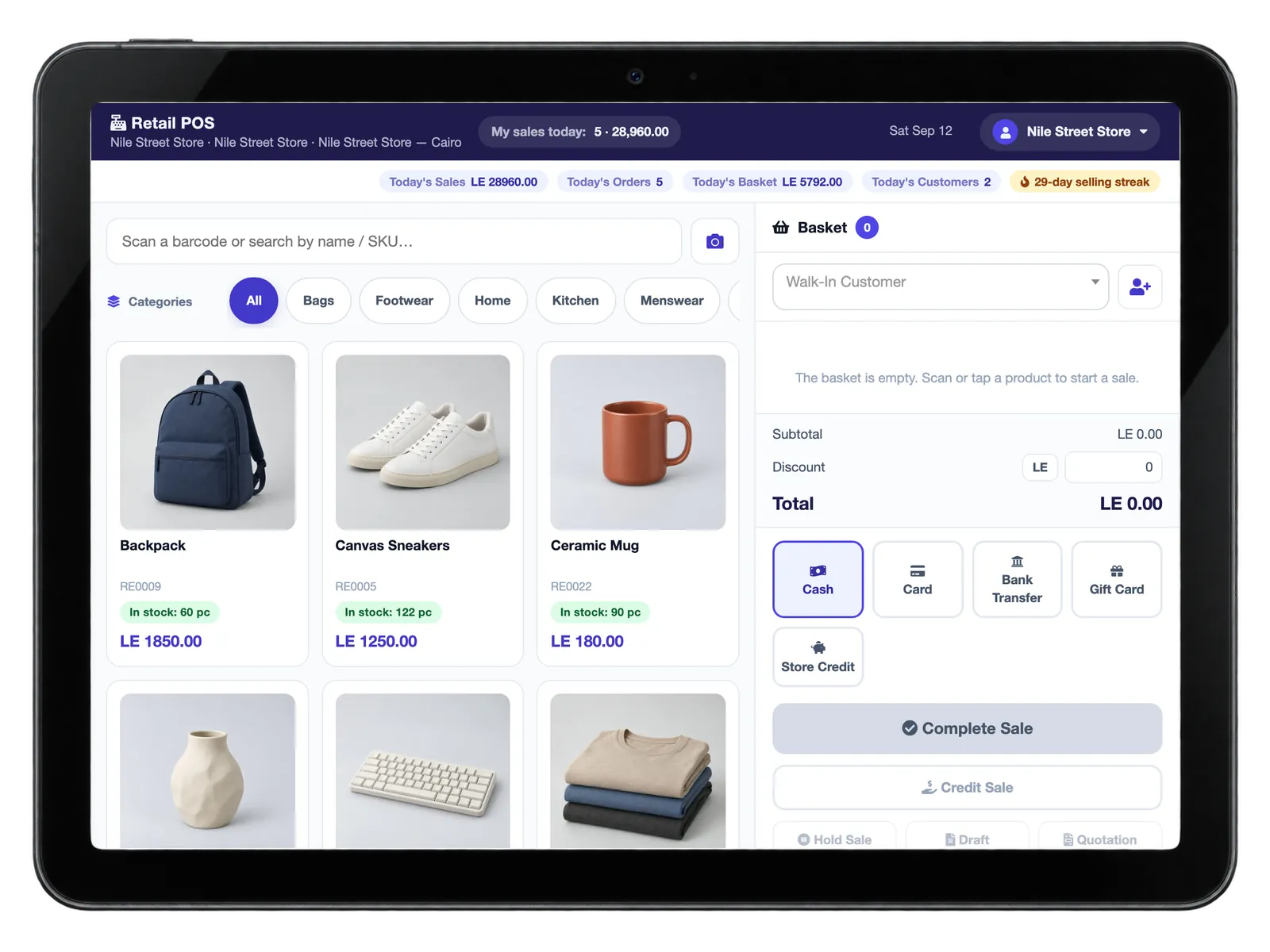 A countertop terminal showing the retail point of sale: a grid of photographed products with prices and stock, and an open basket.